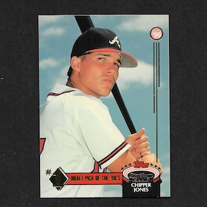 May include: A Topps Stadium Club baseball card featuring Chipper Jones. The card shows a player in a white Atlanta Braves jersey and a black cap with a red brim, holding a black bat. Text on the card reads Draft Pick of the '90s and 90.