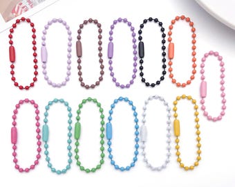 May include: A collection of colorful ball chain keychains in various shades, including red, purple, brown, black, orange, pink, teal, green, blue, white, and yellow. Each keychain features a matching colored clasp.