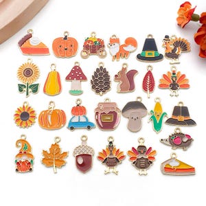 May include: A selection of colourful enamel charms with gold-tone findings. The charms depict various autumn-themed designs, including pumpkins, sunflowers, turkeys, acorns, and pie slices. These charms are suitable for jewellery making or seasonal crafts.