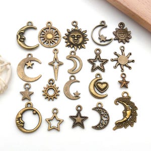 May include: A collection of bronze-colored celestial charms, including moons, stars, and suns. The charms vary in design, with some featuring faces and intricate details. These small pendants are ideal for jewelry making or craft projects.