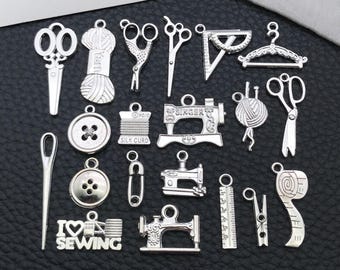 Puede incluir: Una colección de dijes de costura plateados, que incluyen tijeras, botones, máquinas de coser, carretes de hilo y una cinta métrica. Los dijes están dispuestos sobre una superficie oscura, con la frase "I love sewing".