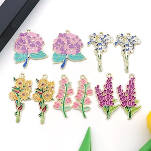Peut inclure: Une collection de breloques florales colorées. Les breloques présentent des détails émaillés dans des tons de violet, rose, jaune et vert, avec des accents métalliques dorés. Chaque breloque a une boucle pour l'attache.