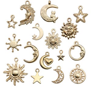 May include: A collection of 17 gold-toned metal charms featuring various celestial designs, including suns, moons, and stars. Some charms have intricate details, such as faces or hearts.