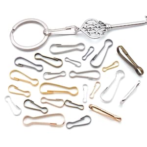 May include: A collection of various metal lobster claw clasps in silver, gold, bronze, and gunmetal tones, featuring different sizes and shapes. One silver-toned key-shaped keychain with a circular ring is attached to a lobster claw clasp.