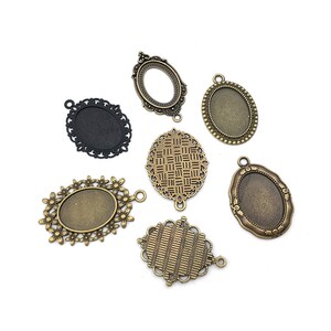 May include: Seven antique gold-toned metal oval-shaped pendant trays with different decorative edges. The trays are designed to hold small items like photos, charms, or other jewelry.