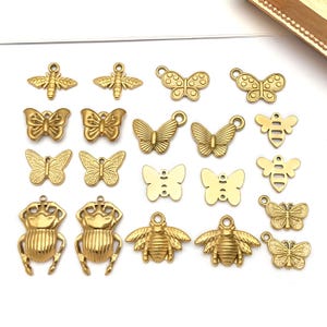 Pode incluir: Uma coleção de pingentes de metal dourado com vários designs de insetos e borboletas. Os pingentes incluem borboletas, abelhas e besouros, cada um com um laço para fixar. Os pingentes são detalhados e têm um acabamento brilhante.
