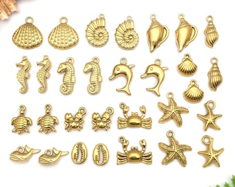 May include: A collection of gold-colored charms in various sea-themed shapes, including seashells, seahorses, dolphins, turtles, crabs, and starfish. Each charm has a small loop for attaching to jewelry or other crafts. The charms are arranged on a white surface.