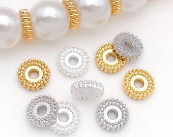 May include: Close-up of jewelry components, including large white faux pearls and small, round spacer beads. The spacer beads are in gold and silver tones, with a beaded edge and a central hole. The components are for jewelry making.