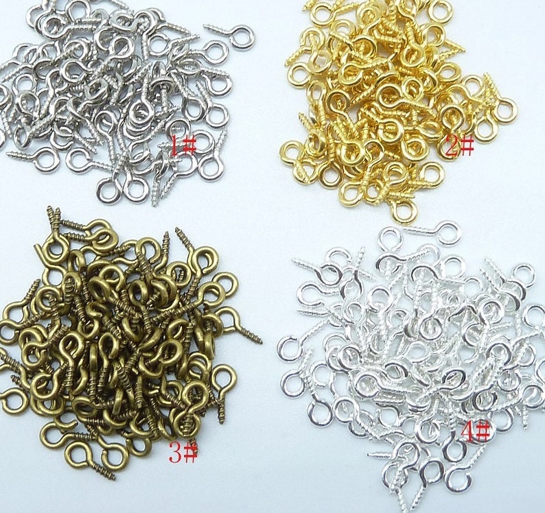 May include: Four piles of screw-back eyelet findings in silver, gold, bronze, and antique silver. Each pile is labelled with a number.