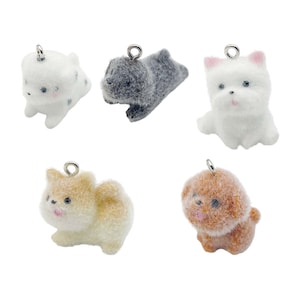 Op de afbeelding: Vijf kleine pluche hondencharms met zilveren springringen. De charms zijn wit, grijs, bruin en wit met zwarte vlekken. De honden zijn in verschillende poses.