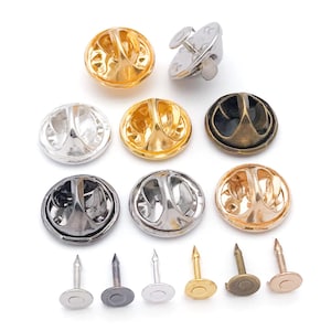 Puede incluir: Una colección de broches redondos de metal en varios colores, incluyendo dorado, plateado y negro. Los broches tienen un diseño texturizado y se muestran con sus respaldos de alfiler. La imagen también incluye varios respaldos de alfiler.