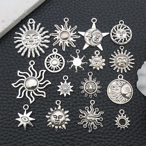Könnte beinhalten: Eine Sammlung silberfarbener Sonnen- und Mondanhänger. Die Anhänger variieren in Größe und Design und zeigen lächelnde Sonnengesichter, sternförmige Strahlen und Monddetails. Ideal für Schmuckherstellung oder Bastelprojekte.