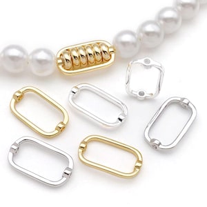 Puede incluir: Una colección de cierres de joyería en tonos dorados y plateados. Los cierres tienen varias formas, incluyendo rectangulares y un cierre en forma de barril con una serie de barras doradas. Un collar de perlas es parcialmente visible en el fondo.