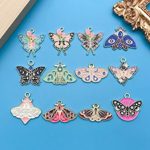 May include: Assortment of 12 gold-tone metal butterfly charms with enamel detailing. The butterflies are in various colors, including pink, blue, green, black, and white. Each charm features a different butterfly design.