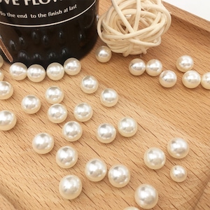 Op de afbeelding: Een close-up van een houten oppervlak met een groot aantal witte parel kralen die eroverheen zijn verspreid. De kralen zijn rond en glad, en ze zijn in een willekeurig patroon gerangschikt.