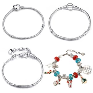 May include: Four silver charm bracelets. Two are simple silver chain bracelets with a heart charm and a round charm. The other two are charm bracelets with a variety of charms including a snowman, a reindeer, a candy cane, a music note, a Christmas tree, and a blue and red bead. One charm has the text "She believed she could so she did."