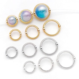 May include: Assortment of gold and silver jump rings with a beaded edge. The jump rings are in various sizes. There are also two pearl-like beads with gold settings.