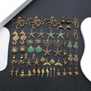 May include: A selection of bronze-coloured sea-themed charms, including starfish, seahorses, octopuses, and shells. Some charms have turquoise accents. The charms are arranged on a black surface, ideal for jewellery making or crafting.