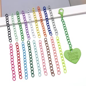 May include: A collection of colorful chain extenders in various hues, including pink, red, blue, green, and brown. A green chain with a heart-shaped tag that reads "Mozto Hiang since 1988" is also present. These are likely jewelry making supplies.