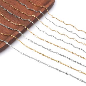 May include: A selection of gold and silver-toned chain necklaces. The chains feature diverse designs, such as twisted, wavy, and link patterns. The necklaces are presented on a wooden surface, highlighting their varied textures and finishes.