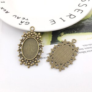 May include: Two antique gold-toned metal pendant trays with oval-shaped glass inserts. One tray features a floral design and the other has a geometric pattern.