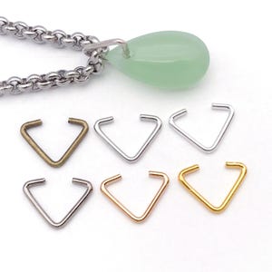 May include: A collection of six metal ear cuffs in various finishes: bronze, silver, rose gold, and gold. A green teardrop-shaped pendant hangs from a silver chain. The ear cuffs are triangular with open ends.