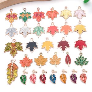 May include: A collection of colorful leaf-shaped charms with gold-tone metal edges. The charms feature various colors, including red, orange, yellow, green, and purple. Each charm has a loop for attaching to jewelry or other crafts.