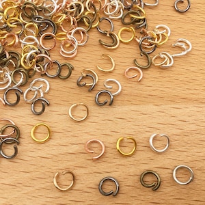 May include: A selection of jump rings in various sizes and colours, including gold, silver, bronze, and black. The jump rings are scattered on a wooden surface.