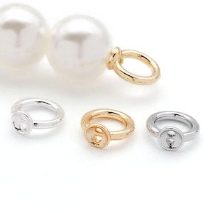 May include: Three jump rings in gold, silver, and white metal. The rings are round and have a small, flat circle in the centre. The rings are used for jewellery making.