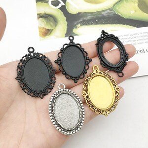 May include: Four oval-shaped metal pendant trays with different finishes: black, gold, and silver. The trays have intricate designs around the edges and are ready for crafting projects.