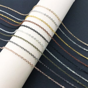 Puede incluir: Surtido de eslabones de cadena en varios colores, incluyendo plata, oro, negro y cobre. Las cadenas están dispuestas en una fila sobre una superficie blanca.