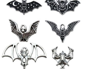 May include: A collection of six silver-toned metal bat charms in various designs. Two charms feature black enamel detailing with celestial patterns, while the others are solid silver-toned metal with intricate wing and body textures.