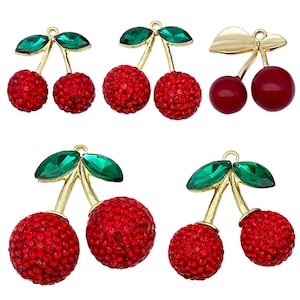 Puede incluir: Una variedad de dijes con forma de cereza. Los dijes presentan cerezas rojas con gemas, con tallos dorados y hojas verdes con forma de gema. Un par tiene cerezas lisas de color rojo oscuro. Adecuado para la fabricación de joyas.