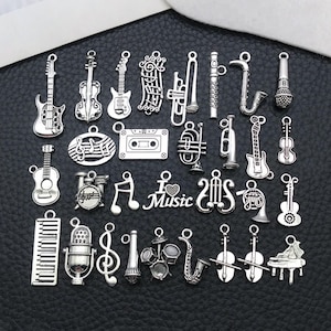 Può includere: Una collezione di ciondoli argentati a tema musicale. I ciondoli includono chitarre, violini, note musicali, una musicassetta, un microfono e vari strumenti. La parola "Music" è presente.