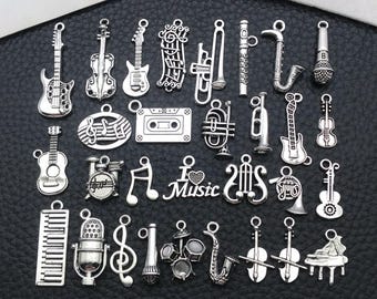 Pode incluir: Uma coleção de pingentes prateados com tema musical. Os pingentes incluem guitarras, violinos, notas musicais, uma fita cassete, um microfone e vários instrumentos. A palavra "Music" também está presente.