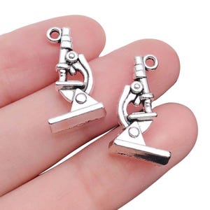 May include: Two silver microscope charm pendants. The charms are detailed and have a vintage look.