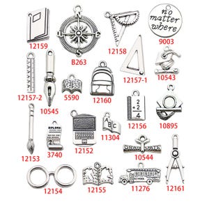 May include: A collection of silver charm pendants with various school-themed designs, including a compass, a ruler, a graduation cap, a book, a pencil, a diploma, a laptop, a school bus, and a pair of glasses. The charms are all silver and have a vintage look.