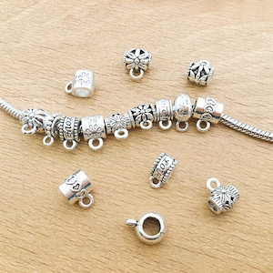 May include: A set of silver-toned metal bead spacers for jewellery making. The spacers feature various designs, including flowers, hearts, and the word "love".