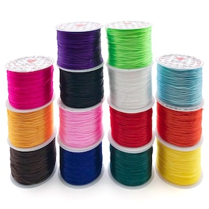Könnte beinhalten: Ein Stapel bunter elastischer Schnurspulen in verschiedenen Farben, darunter Pink, Lila, Grün und Blau. Jede Spule ist sauber aufgewickelt und eignet sich zum Basteln oder für die Schmuckherstellung. Die Spulen sind übereinander gestapelt.
