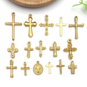 May include: A collection of gold-colored cross charms in various designs. The crosses vary in size and style, with some featuring ornate detailing and others with a simple, classic look. Each charm has a small loop for attaching to a necklace or bracelet.