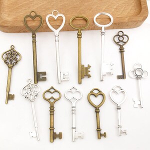 May include: A collection of twelve antique-style skeleton keys in silver and bronze finishes. The keys feature various ornate designs, including hearts, swirls, and geometric shapes.