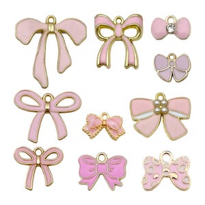May include: Assortment of ten pink and gold bow charms with different designs. The bows are made of metal and have a shiny finish. Some bows have a pearl or rhinestone accent.
