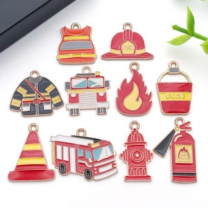 May include: A selection of enamel charms with a firefighter theme. The charms feature a firefighter's helmet, fire engine, flames, fire extinguisher, and other related items. Each charm has a gold-coloured loop for attaching to jewellery or other crafts.