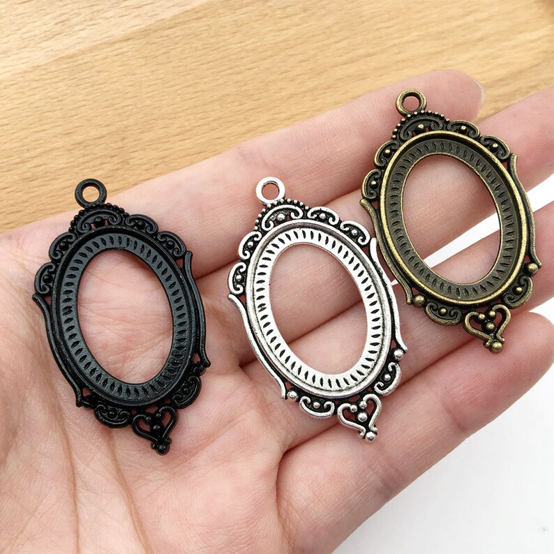 May include: Three oval-shaped metal picture frames with ornate designs. The frames are silver, black, and bronze.
