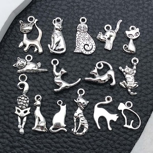 Può includere: Una collezione di ciondoli a forma di gatto color argento in varie pose. I ciondoli includono gatti seduti, in piedi, che si allungano e sdraiati. Ogni ciondolo ha un piccolo anello per il fissaggio a gioielli o altri lavori artigianali.