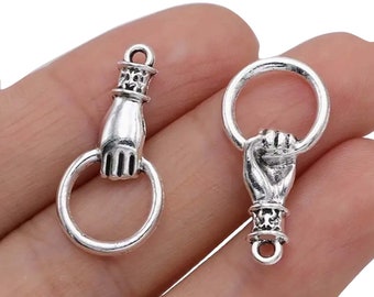May include: Two silver-toned metal charms shaped like a hand holding a ring. The charms are detailed with intricate designs and have a vintage look.