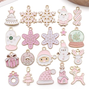 May include: A selection of Christmas-themed charms in pink, white, and gold. The charms feature a Christmas tree, snowflakes, Santa Claus, a mitten, a gift, a donut, a snowman, a reindeer, a star, a snow globe, a wreath, a hat, and a house.