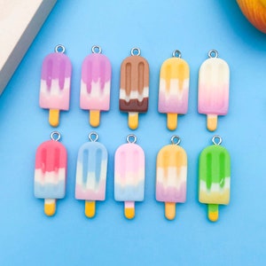 May include: Twelve colorful popsicle charms with silver jump rings. The charms are made of polymer clay and feature different color combinations, including pink, blue, yellow, green, and brown.