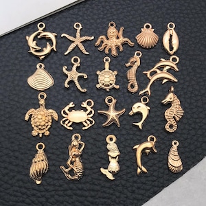 Pode incluir: Uma coleção de pingentes dourados com tema marinho, incluindo golfinhos, estrelas do mar, um polvo, conchas, um cavalo-marinho, uma tartaruga, um caranguejo e uma sereia. Estes pingentes são projetados com um laço na parte superior.