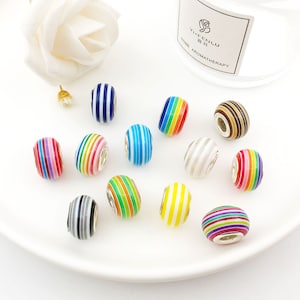 May include: Assortment of colourful striped glass beads with silver accents. The beads are arranged on a white plate.